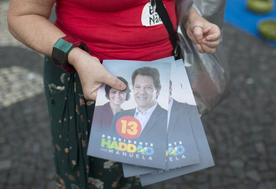 In this Oct. 17, 2018 photo, a campaigner holds a stack of flyers for Workers' Party candidate Fernando Haddad, and wears #NotHim stickers against far-right contender Jair Bolsonaro, in Rio de Janeiro, Brazil. Haddad, the hand-picked successor to jailed former President Luiz Inacio Lula da Silva, is hurt by the reluctance of many to return to power the leftist Worker’s Party, which governed Brazil from 2003 until early 2016. (AP Photo/Beatrice Christofaro)