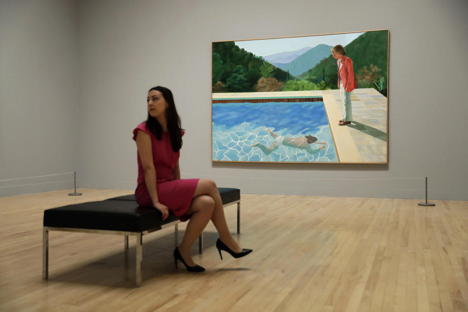 FILE - In this Feb. 6, 2017, file photo, a Tate representative poses for photographs next to British artist David Hockney's "Portrait of an Artist (Pool with Two Figures) during a photo call to promote the largest-ever retrospective of his work at Tate Britain gallery in London. The painting, considered one of Hockney's premier works, was sold at auction by Christie's in New York for $90.3 million. (AP Photo/Matt Dunham, File)