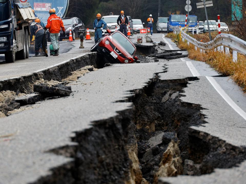 Workers stand on a road where a car is stuck on a broken road after an earthquake in Japan