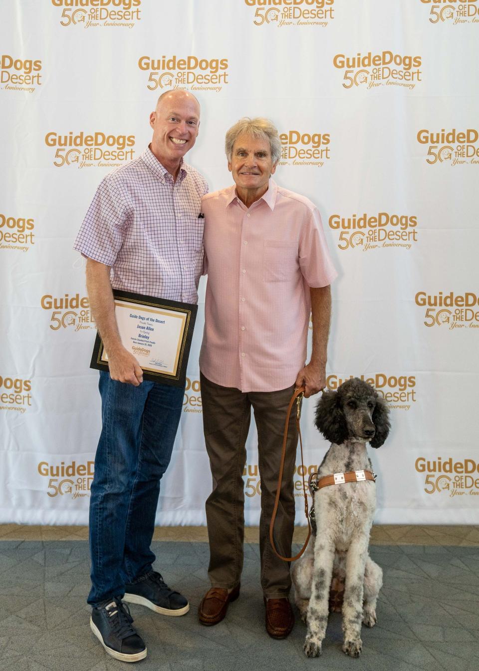 Puppy raiser Jason Allen (left) poses with student Rocky Camp and Brinley, a female parti standard poodle, at the Guide Dogs of the Desert graduation ceremony on May 21, 2022.