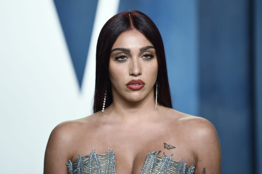 A woman with long brownish red hair posing in dark lipstick and a silver dress