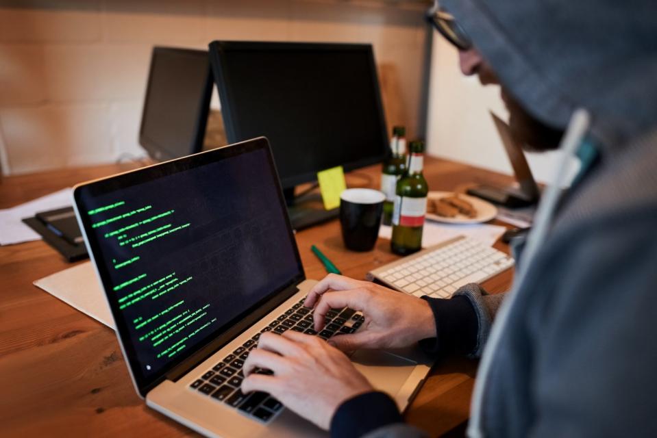 Person in hoodie writing code on a laptop computer on a table.