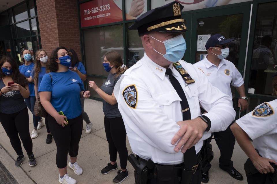 Tanning salon workers, left, stand behind police outside the Staten Island business, Thursday, May 28, 2020, in New York. Owner Bobby Catone opened the salon briefly Thursday morning in defiance of a law requiring non-essential businesses to remain closed during the coronavirus pandemic. (AP Photo/Mark Lennihan)