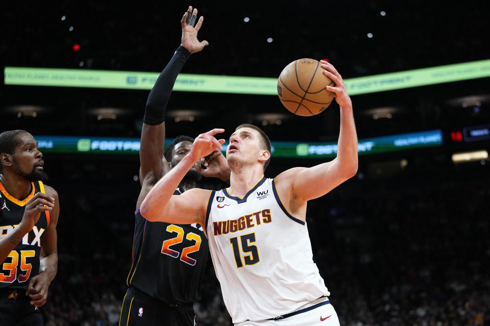 Denver Nuggets center Nikola Jokic (15) shoots over Phoenix Suns center Deandre Ayton (22) during the second half of Game 4 of an NBA basketball Western Conference semifinal game, Sunday, May 7, 2023, in Phoenix. The Suns defeated the Nuggets 129-124. (AP Photo/Matt York)