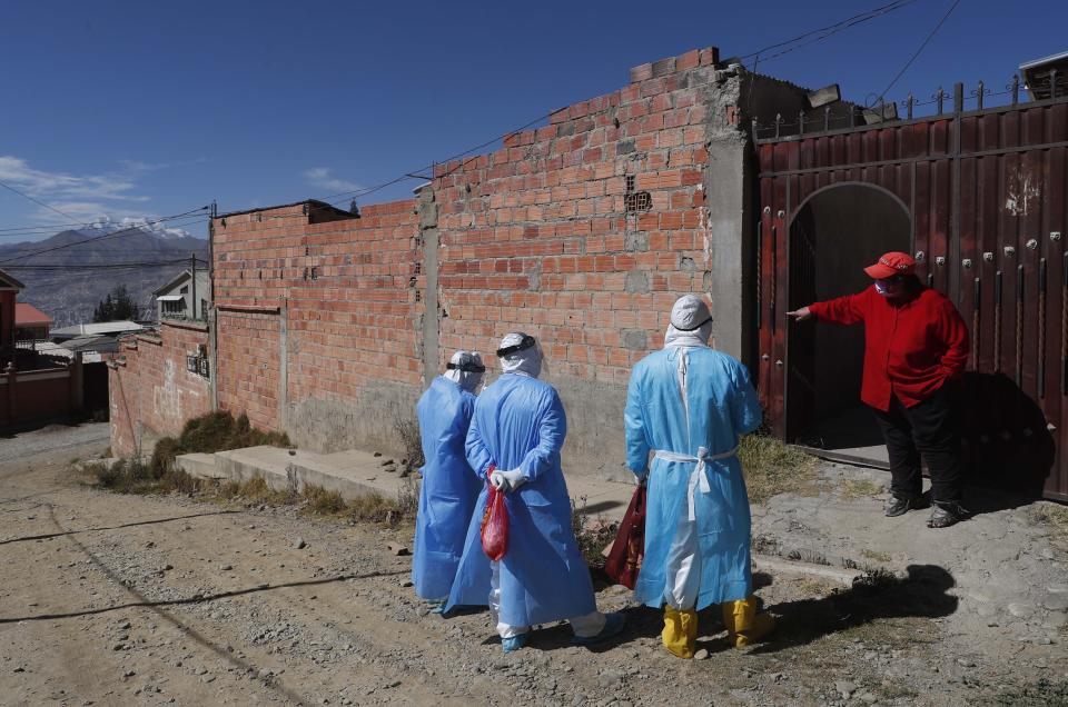 Healthcare workers dressed in full protective gear speak with a woman during a house-to-house coronavirus testing drive in Villa El Rosal, on the outskirts of La Paz, Bolivia, Sunday, July 12, 2020. Bolivia’s Institute of Forensic Investigations said that nationally from April 1 through July 19, its workers had recovered 3,016 bodies of people in possible COVID-19 cases. (AP Photo/Juan Karita)