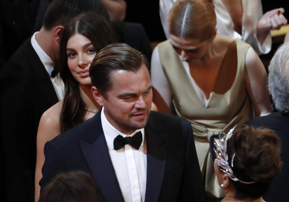 Leonardo DiCaprio and Camila Morrone together at 92nd Academy Awards, Camila smiling up at the camera from behind Leo as he greets another guest