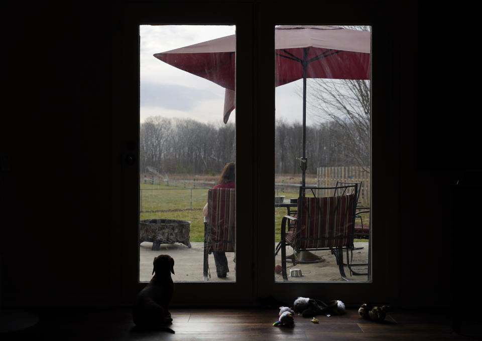 Keri Wegg sits on the patio and talks with medical personnel as her dachshund, Arlo, waits for her return inside their Westfield, Ind., home on Tuesday, March 23, 2021. (AP Photo/Charles Rex Arbogast)