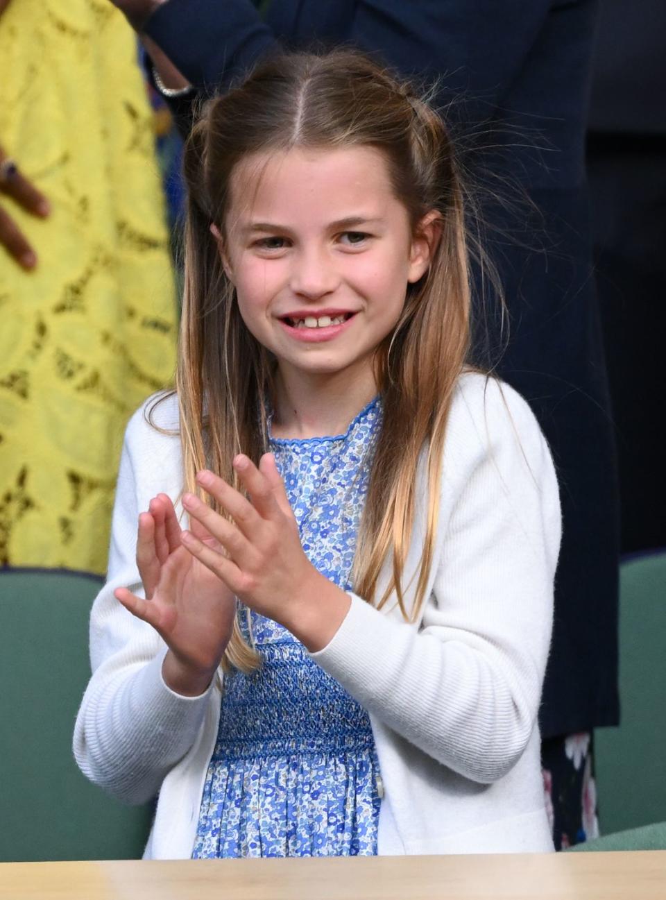 princess charlotte claps her hands and smiles as she stands, she wears a white long sleeve sweater and blue floral dress