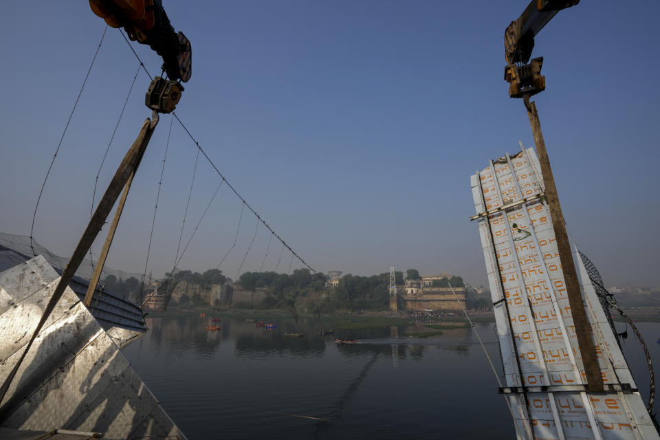 Workers use machinery to remove the debris of a pedestrian bridge that collapsed in Morbi town of western state Gujarat, India, Monday, Oct. 31, 2022. The century-old cable suspension bridge collapsed into the river Sunday evening, sending hundreds plunging in the water in one of the country's worst accidents in years. (AP Photo/Ajit Solanki)