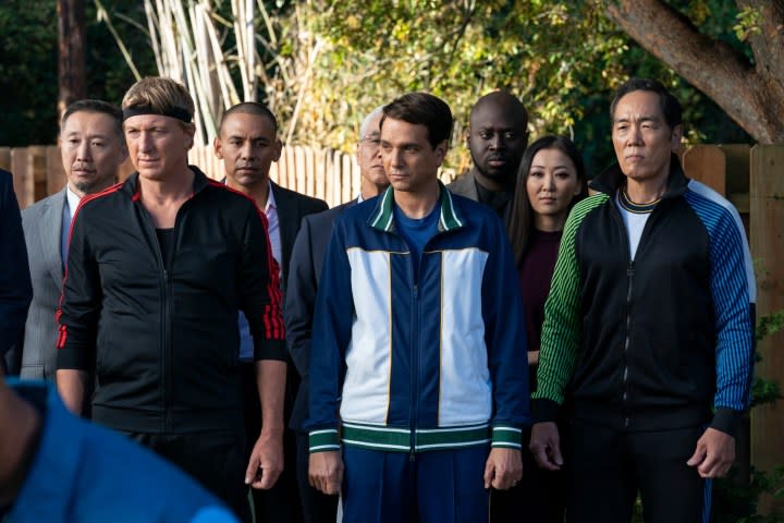 William Zabka, Ralph Macchio, and Yuji Okumoto stand in track suits in a scene from Cobr Kai season 5.