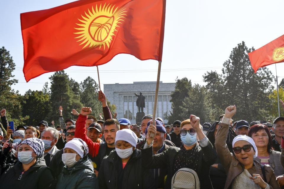 Protesters react waving Kyrgyz national flags as they wait for Kyrgyz Prime Minister Sadyr Zhaparov speech in front of the government building with a statue of Vladimir Lenin in the background in Bishkek, Kyrgyzstan, Wednesday, Oct. 14, 2020. Kyrgyzstan's embattled president has discussed his possible resignation with his newly appointed prime minister in a bid to end the political crisis in the Central Asian country after a disputed parliamentary election. President Sooronbai Jeenbekov held talks with Prime Minister Sadyr Zhaparov a day after refusing to appoint him to the post over concerns whether parliament could legitimately nominate him. (AP Photo/Vladimir Voronin)