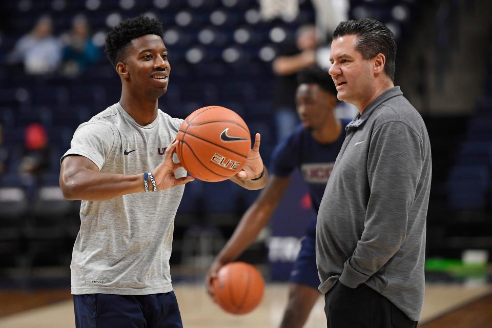 Connecticut student manager Justin Eaddy passes a ball to players warming up as assistant coach Tom Moore looks on before a game in 2020.
