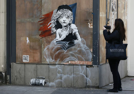 A woman films a new graffiti mural attributed to Banksy, opposite the French embassy in London, Britain January 25, 2016. REUTERS/Stefan Wermuth