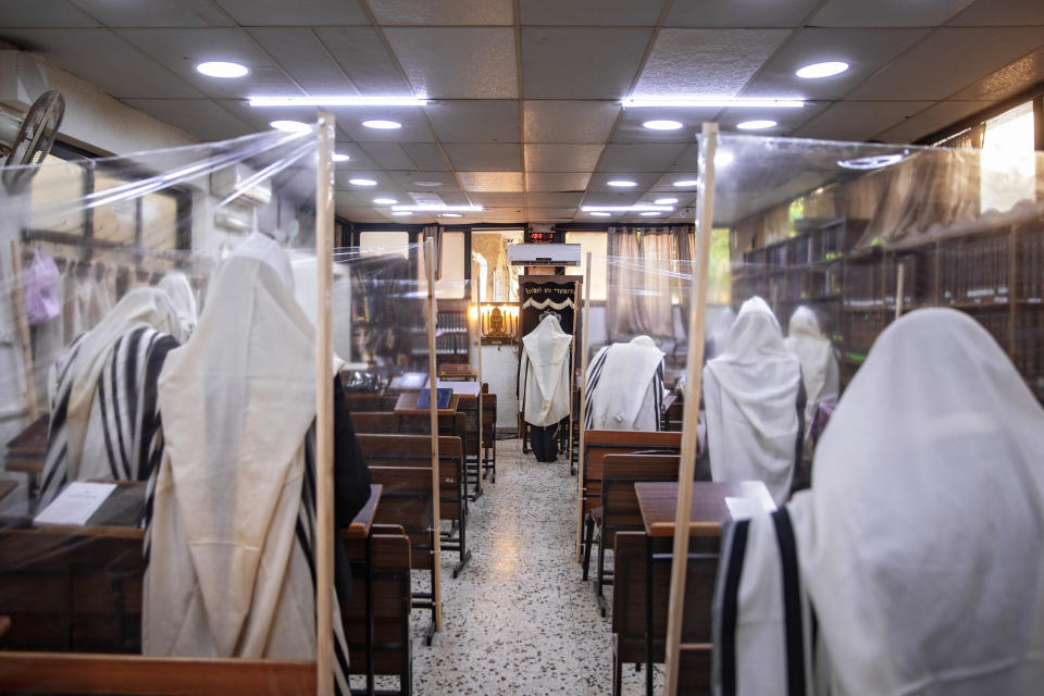 Ultra-Orthodox Jews praying in a synagogue separated by plastic partitions, follow new government measures to help stop the spread of the coronavirus, in Bnei Brak, Israel, Friday, Sept 18, 2020. Israel is set to go back into a three-week lockdown later Friday to try to contain a coronavirus outbreak that has steadily worsened for months as its government has been plagued by indecision and infighting. The closures coincide with the Jewish High Holidays, when people typically visit their families and gather for large prayer services. (AP Photo/Oded Balilty)