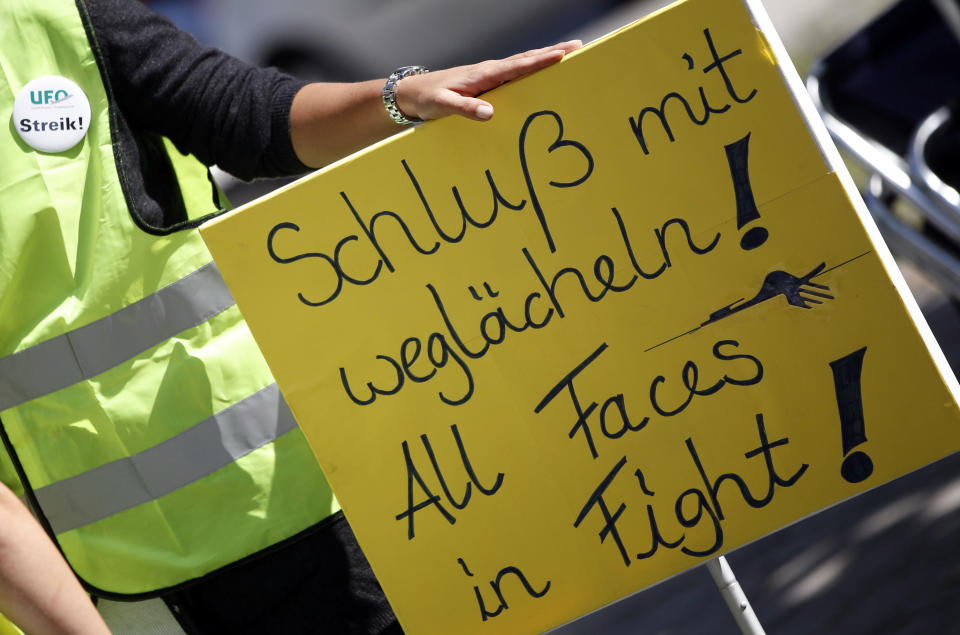 A Lufthansa cabin crew member holds a poster during a demonstration as flight attendants of German Lufthansa airline went on an 24-hour-strike for higher wages at the airport in Munich, southern Germany, on Friday, Sept. 7, 2012. First sentence on the poster reads "Finish smiling away". (AP Photo/Matthias Schrader)