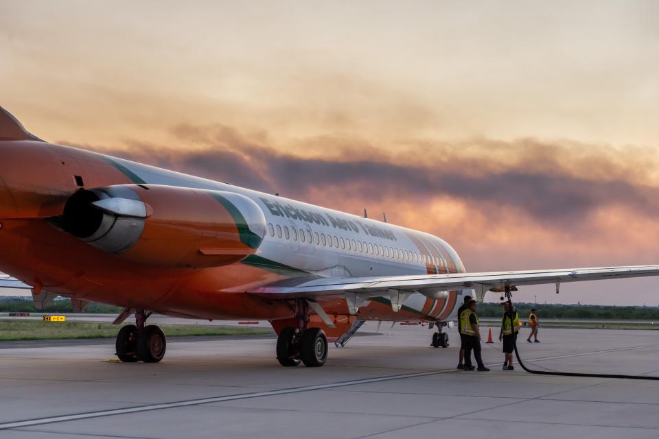 Workers at Abilene Regional Airport refuel a firefighting airplane, with smoke from a wildfire near View seen in the background.