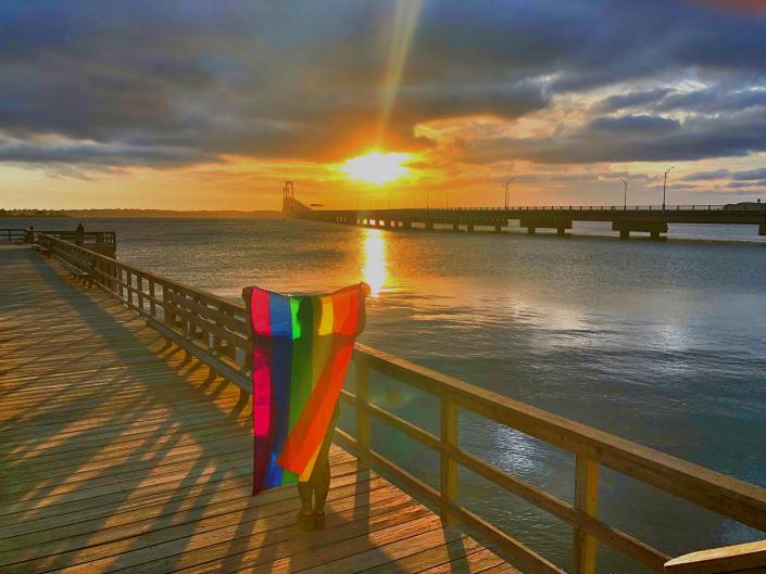 A person holds a Pride flag as the sun sets over the Newport Pell Bridge.