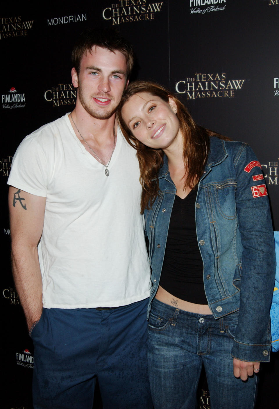 Chris Evans in a tee and pants next to Jessica Biel who's wearing a denim outfit and leaning her head against Chris's shoulder