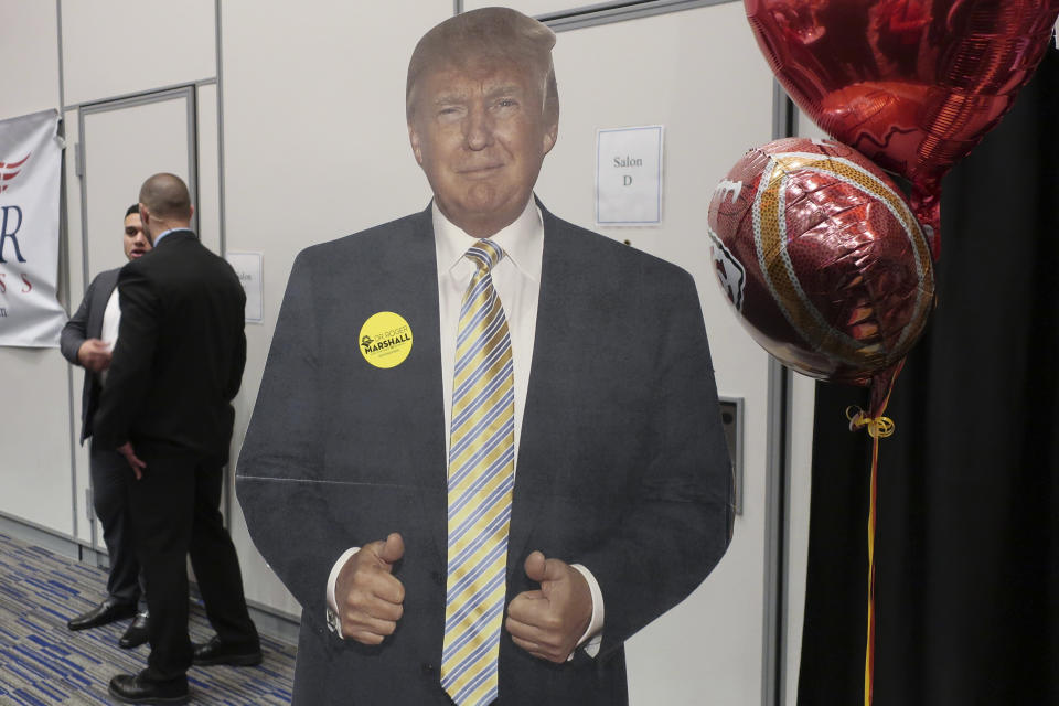 In this Friday, Jan. 31, 2020, photo, a cardboard cutout of President Donald Trump stands at a table for U.S. Rep. Roger Marshall, R-Kan., at a Kansas Republican Party convention in Olathe, Kan. Marshall is running for the U.S. Senate and touting what he calls an "incredible relationship" with the president. (AP Photo/John Hanna)