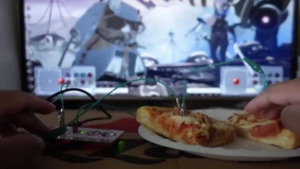A video game controller connected to slices of pizza on a white paper plate in front of a TV