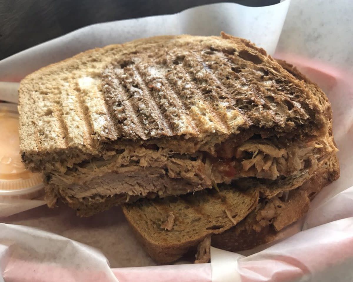 Kalua Pork Sandwich on with a cup of dipping sauce, on white serving paper on a red tray, 808 Deli, Kihei, Hawaii, on a dark table