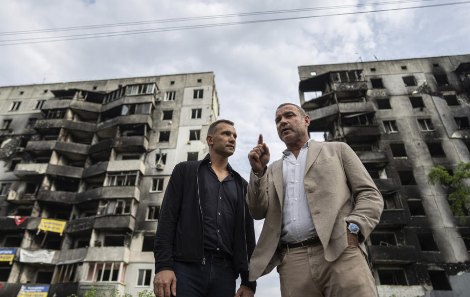 El exfutbolista y entrenador de la selección nacional de Ucrania Andriy Shevchenko, izquierda, y el actor estadounidense Liev Schreiber hablan con medios de comunicación frente a un edificio destruído por la ofensiva rusa en Borodianka, cerca de Kiev, Ucrania, el 15 de agosto de 2022. (Foto AP/Evgeniy Maloletka)