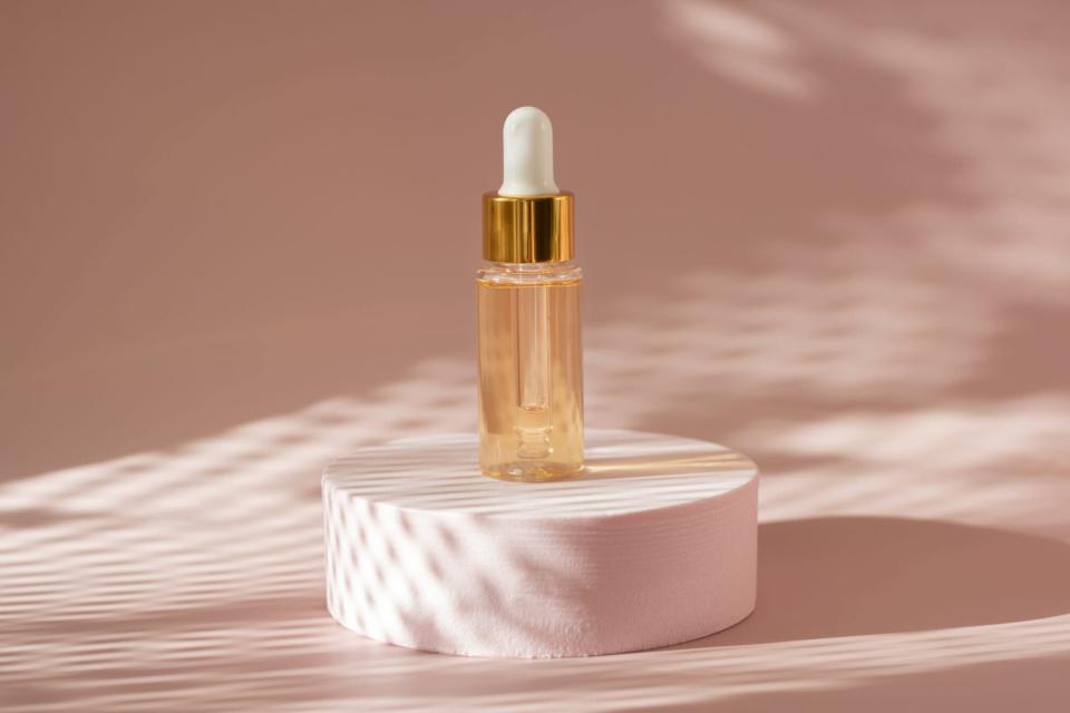 gold beauty serum in a pipette bottle on a pink podium with shadows