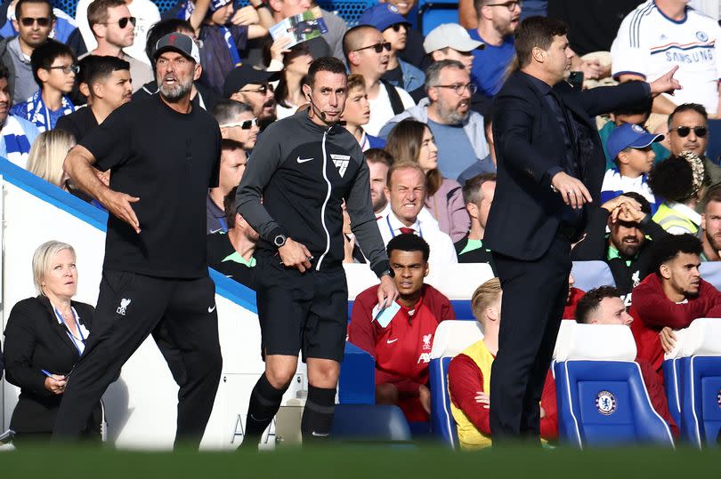 Fourth Official David Coote (C) stands betweeen Liverpool's German manager Jurgen Klopp (L) and Chelsea's Argentinian head coach Mauricio Pochettino during the English Premier League football match between Chelsea and Liverpool at Stamford Bridge in London on August 13, 2023. (Photo by HENRY NICHOLLS / AFP) / RESTRICTED TO EDITORIAL USE. No use with unauthorized audio, video, data, fixture lists, club/league logos or 'live' services. Online in-match use limited to 120 images. An additional 40 images may be used in extra time. No video emulation. Social media in-match use limited to 120 images. An additional 40 images may be used in extra time. No use in betting publications, games or single club/league/player publications. /  (Photo by HENRY NICHOLLS/AFP via Getty Images)