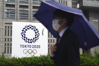 A man wearing a protective mask to help curb the spread of the coronavirus walks in the rain past a banner of Tokyo 2020 Olympic Games Thursday, May 13, 2021, in Tokyo. The Japanese capital confirmed more than 1,000 new coronavirus cases on Thursday. (AP Photo/Eugene Hoshiko)