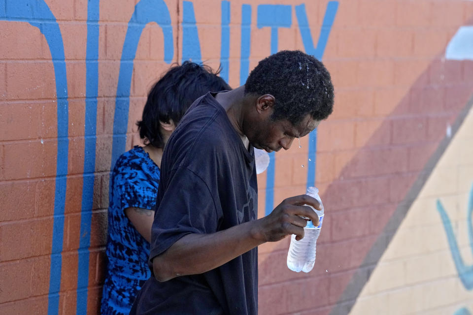 People who are homeless try to cool down with chilled water outside the Justa Center, a day center for homeless people 55 years and older, Friday, July 14, 2023, in downtown Phoenix. During the cooler months, the center stays open until 2 p.m. but has been staying open to at least 5:30 p.m. most days during the current heat spell. The center, located a few blocks from the city's largest homeless shelter, has also been serving as an official hydration station where anyone can stop to get up to two ice-cold bottles of water for free. (AP Photo/Matt York)