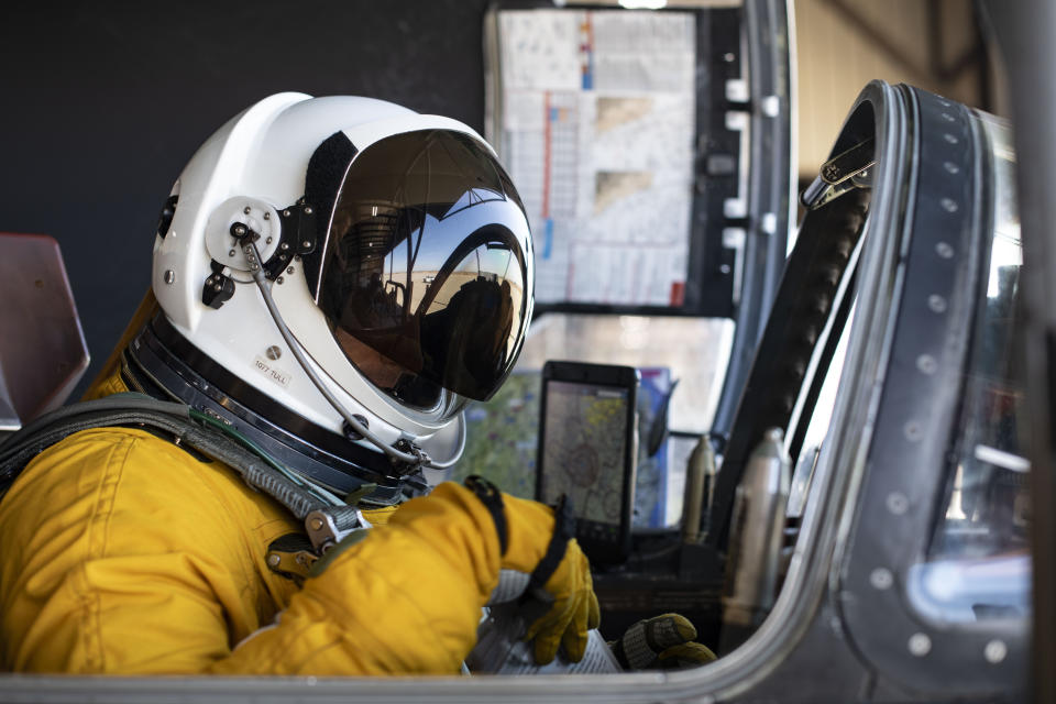 A pilot in a helmet and orange space suit sits in an aircraft cockpit