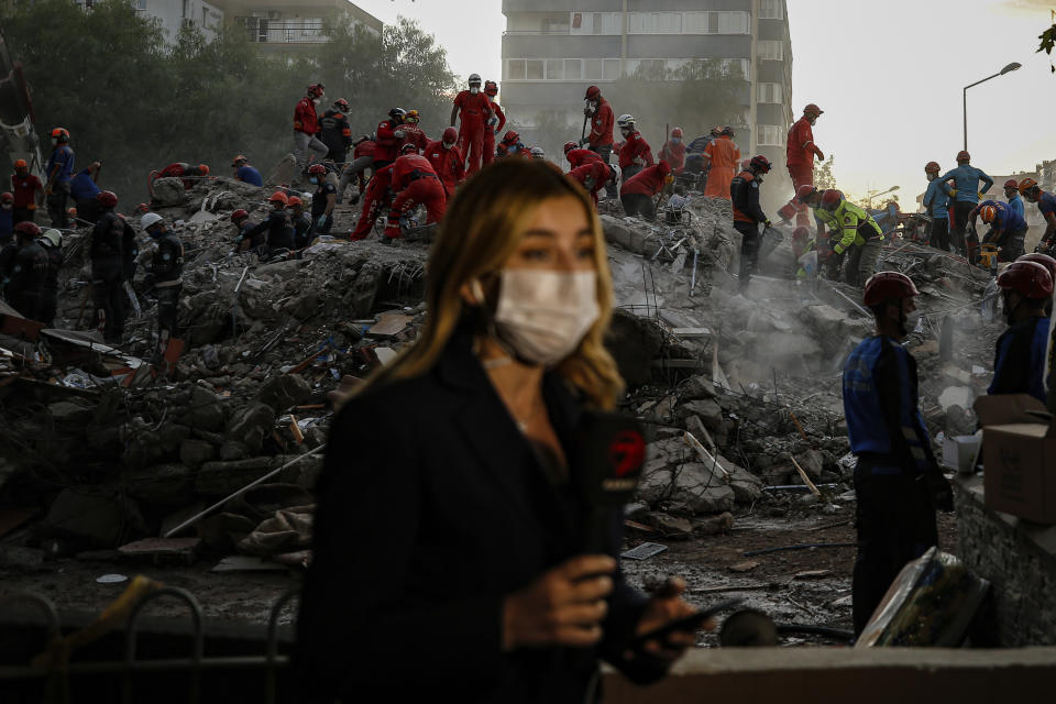 A TV journalist broadcasts from the scene as members of rescue services search for survivors in the debris of a collapsed building in Izmir, Turkey, Monday, Nov. 2, 2020. In scenes that captured Turkey's emotional roller-coaster after a deadly earthquake, rescue workers dug two girls out alive Monday from the rubble of collapsed apartment buildings three days after the region was jolted by quake that killed scores of people. Close to a thousand people were injured. (AP Photo/Emrah Gurel)