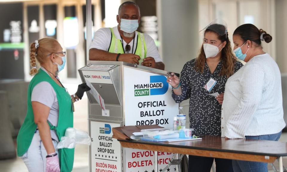 Poll workers help a voter put their mail-in ballot in an official Miami-Dade county ballot drop box on Tuesday in Miami, Florida.