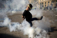 A man kicks away a tear gas canister during a yellow vest demonstration in Paris, Saturday, April 20, 2019. French yellow vest protesters are marching anew to remind the government that rebuilding the fire-ravaged Notre Dame Cathedral isn't the only problem the nation needs to solve. (AP Photo/Francisco Seco)