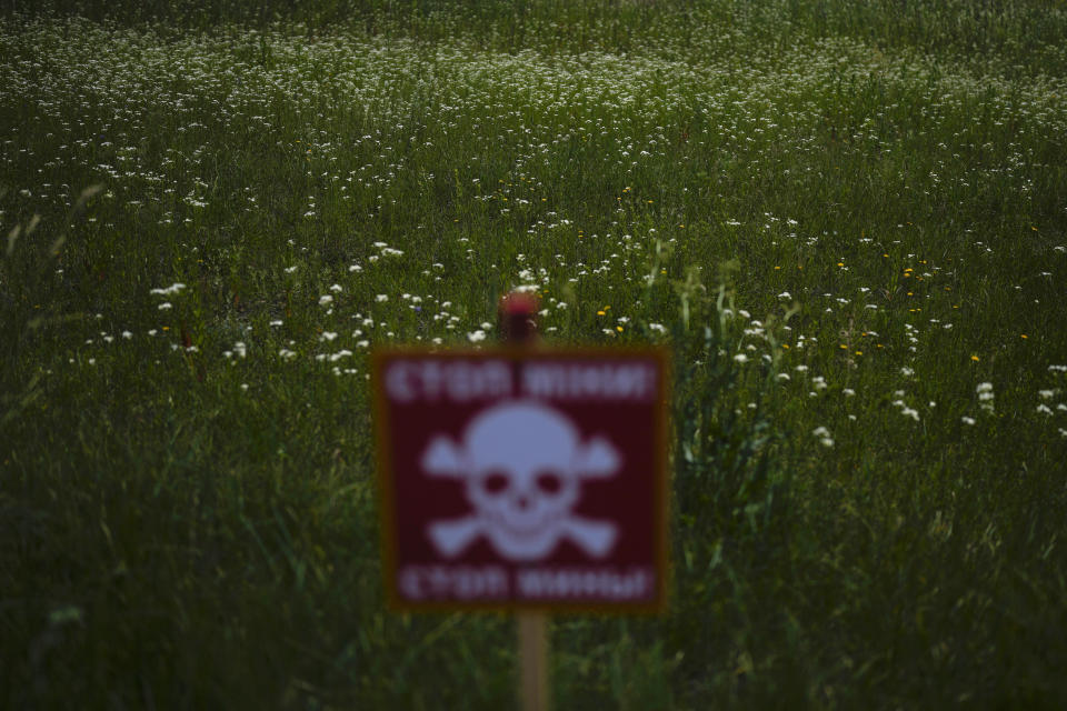 A danger sign warning about land mines is posted in a field blanketed with wildflowers near Lypivka, on the outskirts of Kyiv, Ukraine, Tuesday, June 14, 2022. Russia's invasion of Ukraine is spreading a deadly litter of mines, bombs and other explosive devices that will endanger civilian lives and limbs long after the fighting stops. (AP Photo/Natacha Pisarenko)