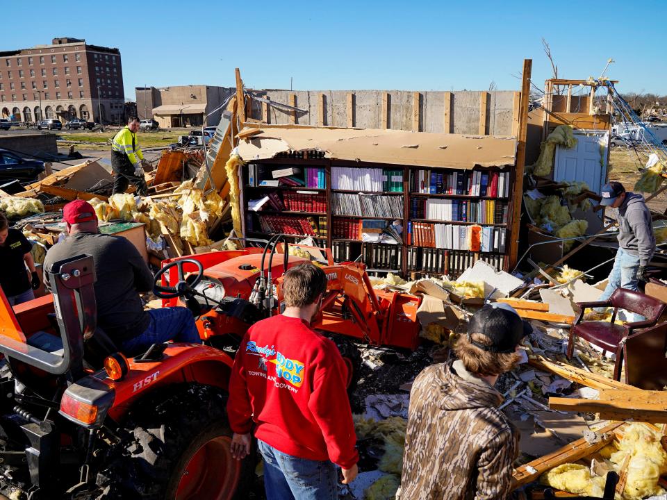 A lone bookshelf stands amid the rubble as people pick through and clean debris after a devastating outbreak of tornadoes ripped through several U.S. states, in Mayfield, Kentucky, U.S., December 12, 2021 (REUTERS)