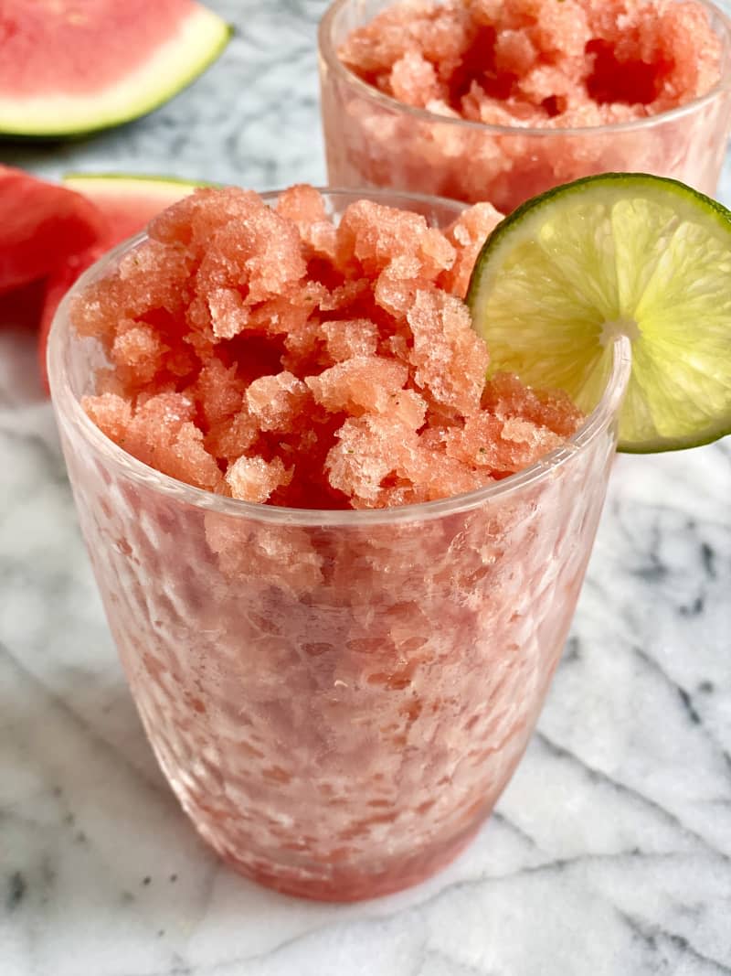 Photograph of watermelon granita in a glass cup with lime slice.