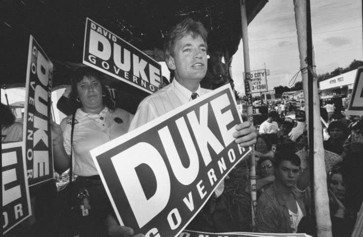 Person at a political rally holding a "DUKE for GOVERNOR" sign with supporters in the background