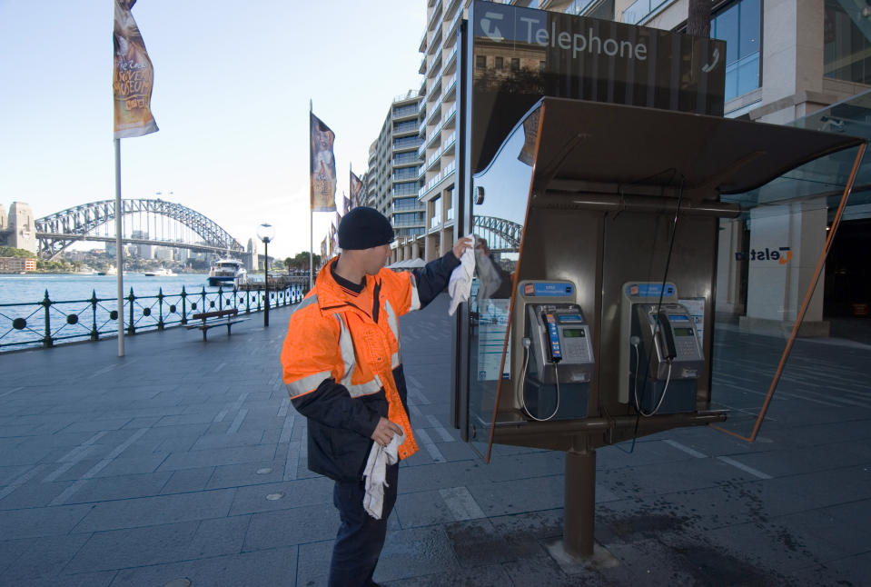 A cleaner working on a Telstra phone booth at Circular Quay, Sydney, Australia. (Photographer: Gillianne Tedder/Bloomberg News.)