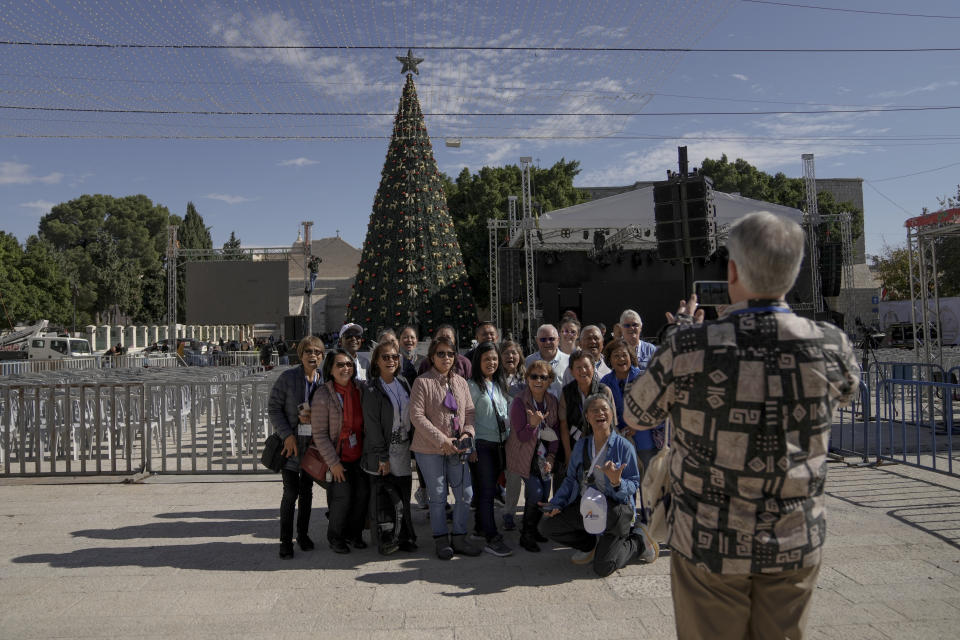 ourists take pictures with the Christmas tree in Manger Square, adjacent to the Church of the Nativity, traditionally believed by Christians to be the birthplace of Jesus Christ, ahead of Christmas, in the West Bank city of Bethlehem, Saturday, Dec. 3, 2022. Business in Bethlehem is looking up this Christmas as the traditional birthplace of Jesus recovers from a two-year downturn during the coronavirus pandemic. Streets are already bustling with visitors, stores and hotels are fully booked and a recent jump in Israeli-Palestinian fighting appears to be having little effect on the vital tourism industry. (AP Photo/ Mahmoud Illean)