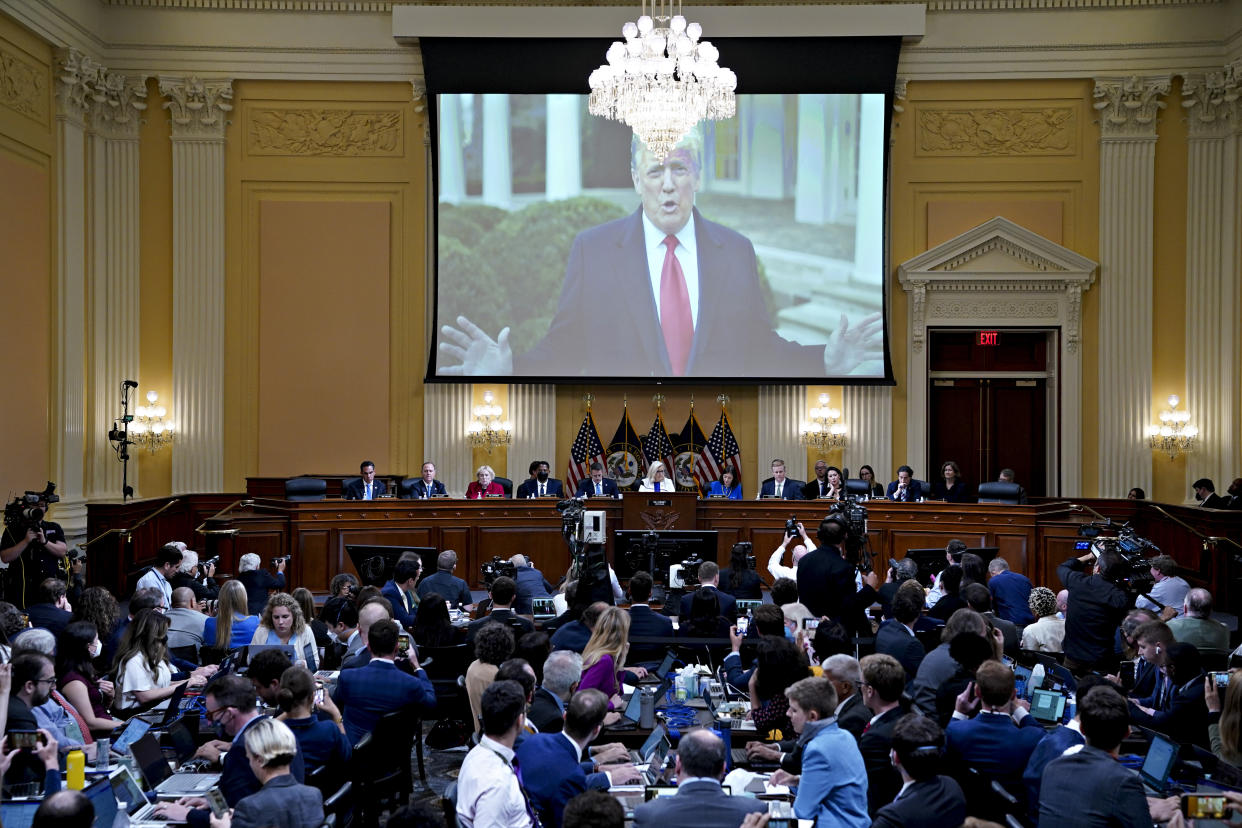 A video of former President Donald Trump is played on a screen above seated members of the Jan. 6 select committee and dozens of other people at tables before them.
