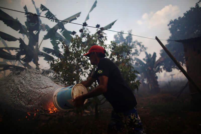 Rosalino de Oliveira throws water trying protect their house as the fire approaches in area of Amazon rainforest, near Porto Velho