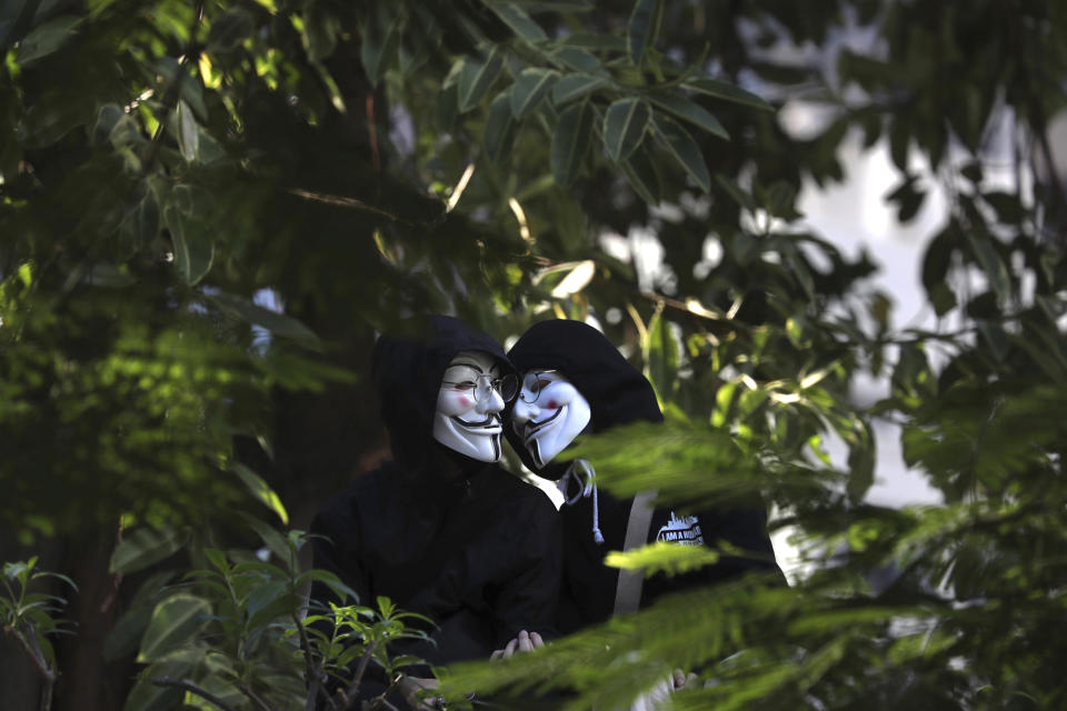 Protesters wear Guy Fawkes masks as they stand in a greenery area during a rally for students and elderly pro-democracy demonstrators in Hong Kong, Saturday, Nov. 30, 2019. Hundreds of Hong Kong pro-democracy activists rallied Friday outside the British Consulate, urging the city's former colonial ruler to emulate the U.S. and take concrete actions to support their cause, as police ended a blockade of a university campus after 12 days. (AP Photo/Ng Han Guan)
