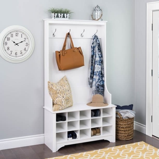 White entryway storage with hooks holding a bag and scarf, shelves with shoes, and a bench with cushions