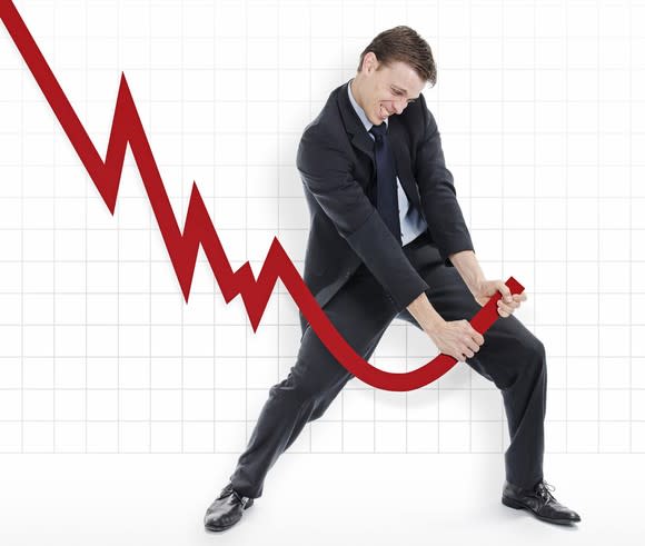 Man in suit struggling to reverse the course of a large downward sloping chart.