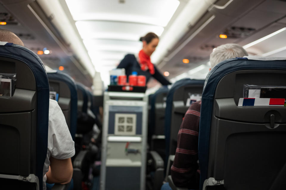 Rear view of people flying in the airplane with flight attendant serving refreshment.