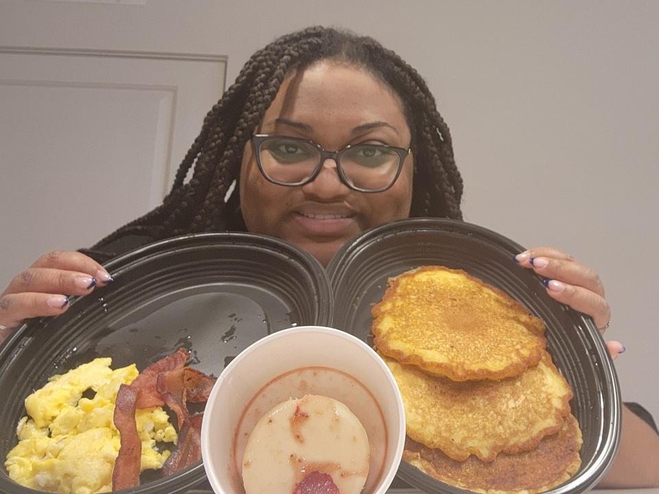 The writer poses with takeout containers of pancakes, cheesecake, bacon, and eggs from Cracker Barrel