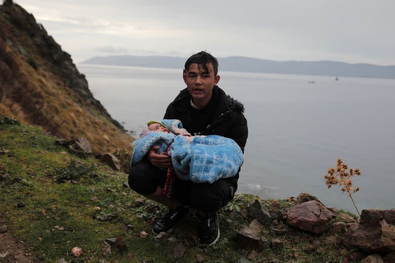 A young man holds a baby as migrant arrive on a beach near the village of Skala Sikamias, after crossing part of the Aegean Sea from Turkey to the island of Lesbos