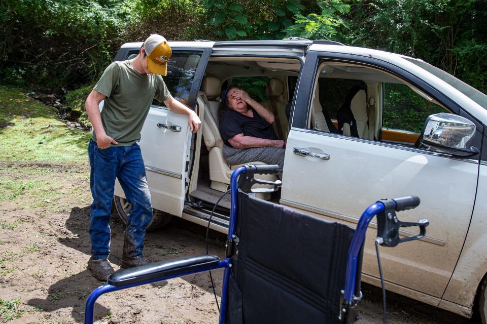 Wendy Fields holds her hand to her face in pain after being helped through the mud and into a van by family and neighbors on Saturday July 30, 2022 in Jenkins, Kentucky. Fields spent the previous three days in the upper level of her home with a broken hip, unable to make it downstairs and out to safety.