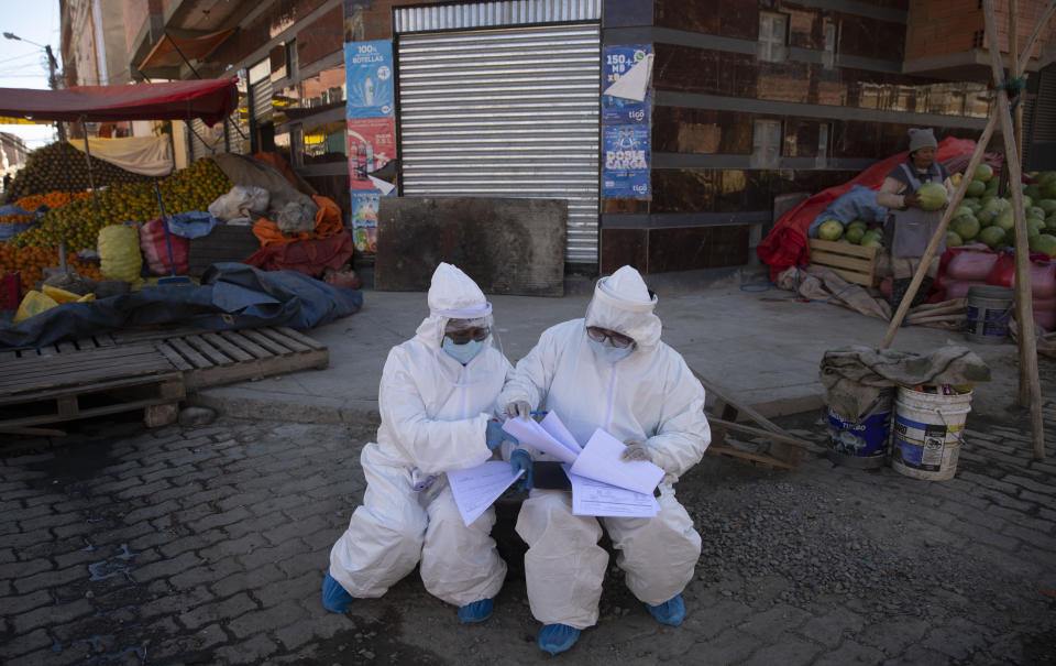 Healthcare workers dressed in full protective gear organize their documents of data they have collected during a house-to-house new coronavirus testing drive, in the Villa Dolores neighborhood of El Alto, Bolivia, Saturday, July 18, 2020. (AP Photo/Juan Karita)